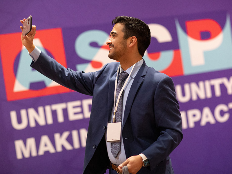 Young man takes a selfie in front of an ASCP sign
