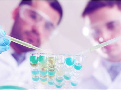 2 men holding pipettes and wearing goggles inside a lab